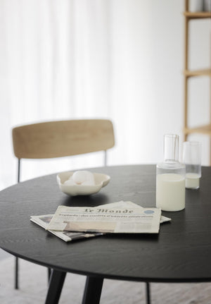 Minimalistiskt matbord i svart med stol, karaff med mjölk, skål och tidning i ljust skandinaviskt kök