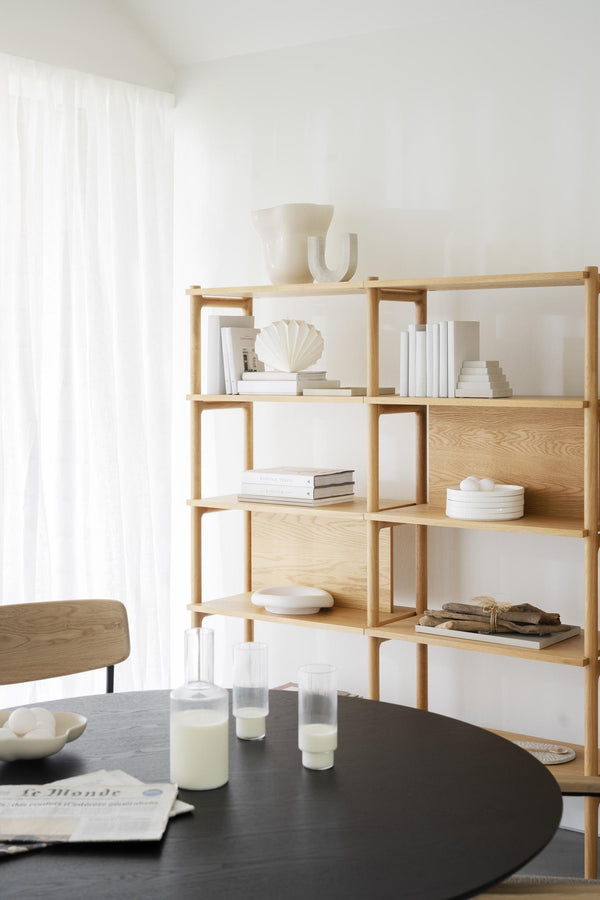 Ljust vardagsrum med bokhylla i ljust trä, svart runt bord och minimalistisk inredning i beige toner