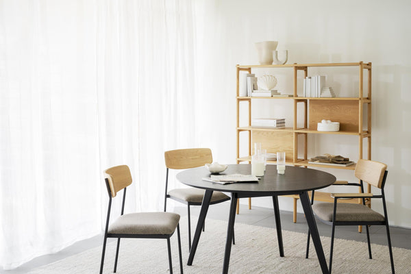 Matbord i svart med fyra stolar och bokhylla i ljust trä i modern skandinavisk matsal