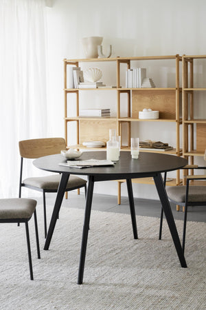Runt matbord i svart trä med matchande stolar och ljus bokhylla i ek i skandinavisk matsal