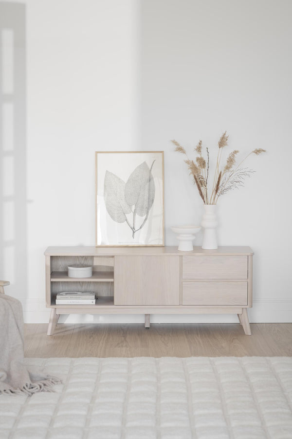 Ljust sideboard i trä med skjutdörr och lådor, dekorerat med ram och torkade blommor i skandinavisk stil