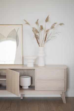 Ljust träskåp med vita vaser och torkade gräs i skandinavisk inredningsstil