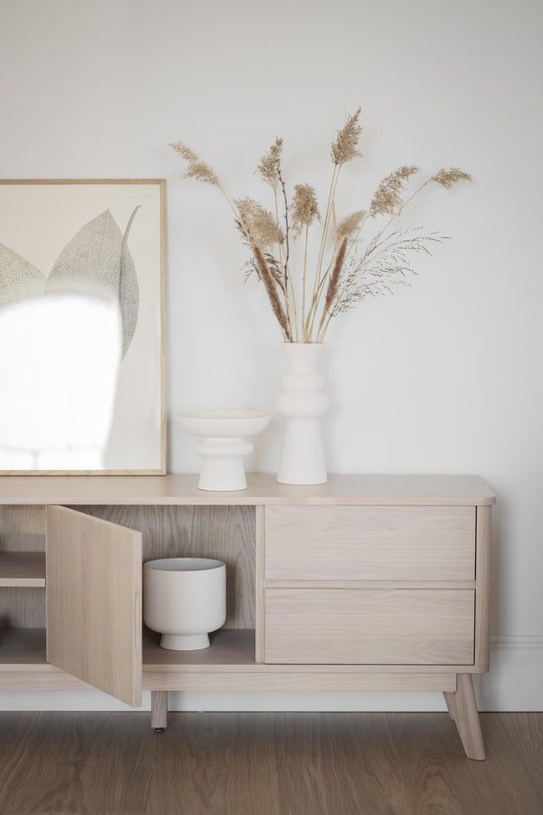 Ljust träskåp med vita vaser och torkade gräs i skandinavisk inredningsstil