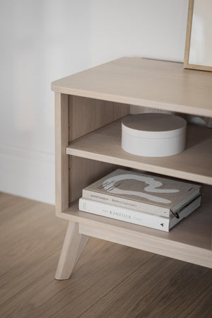 Sängbord i ljust trä med två öppna hyllplan, dekorerat med böcker och en vit ask