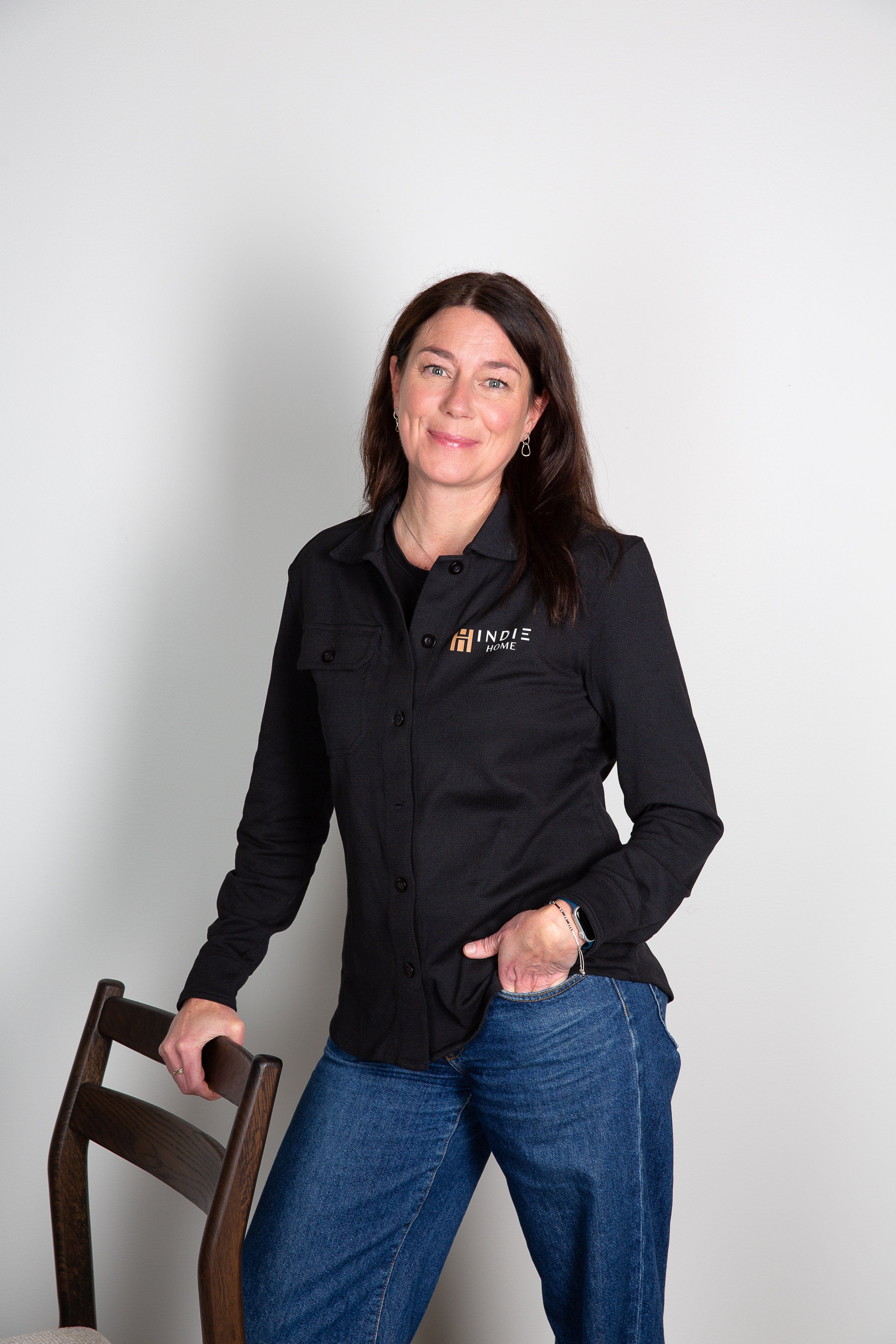 Kvinna i svart skjorta med Incit Home-logga och blå jeans lutar mot stol