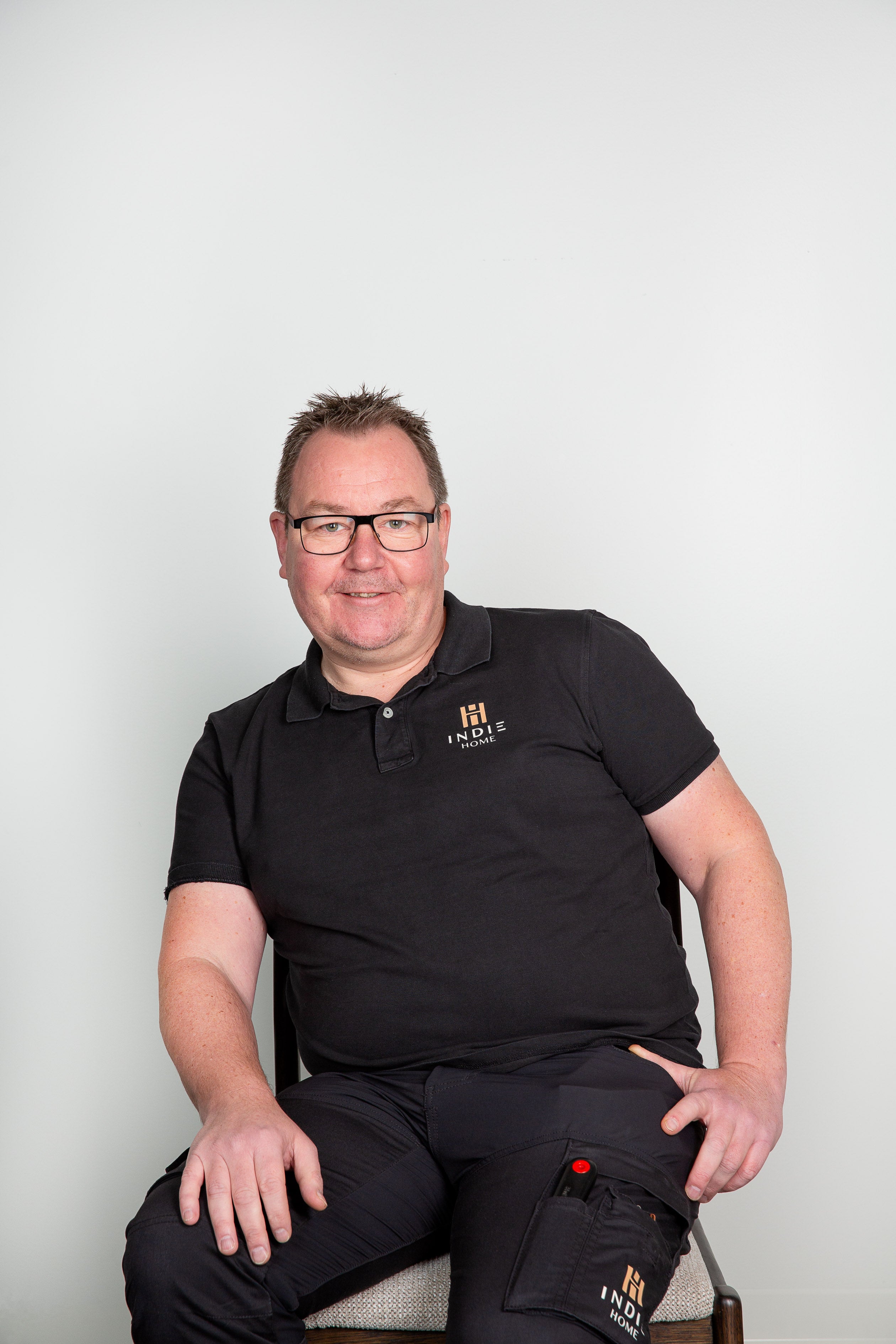 Man i svart piké med Indie Home-logotyp sitter leende mot vit bakgrund