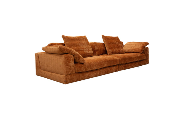 Stor orange soffa i sammet med lösa dynor och låg profil, vinklad vy från sidan