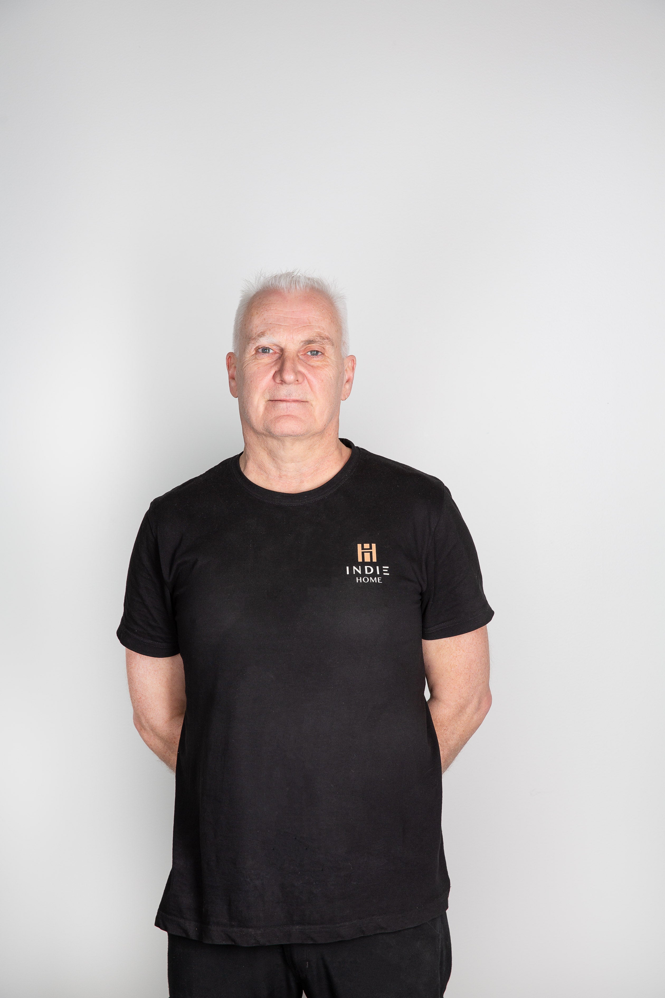 Man i svart t-shirt med INDIE HOME logotyp i guld på bröstet