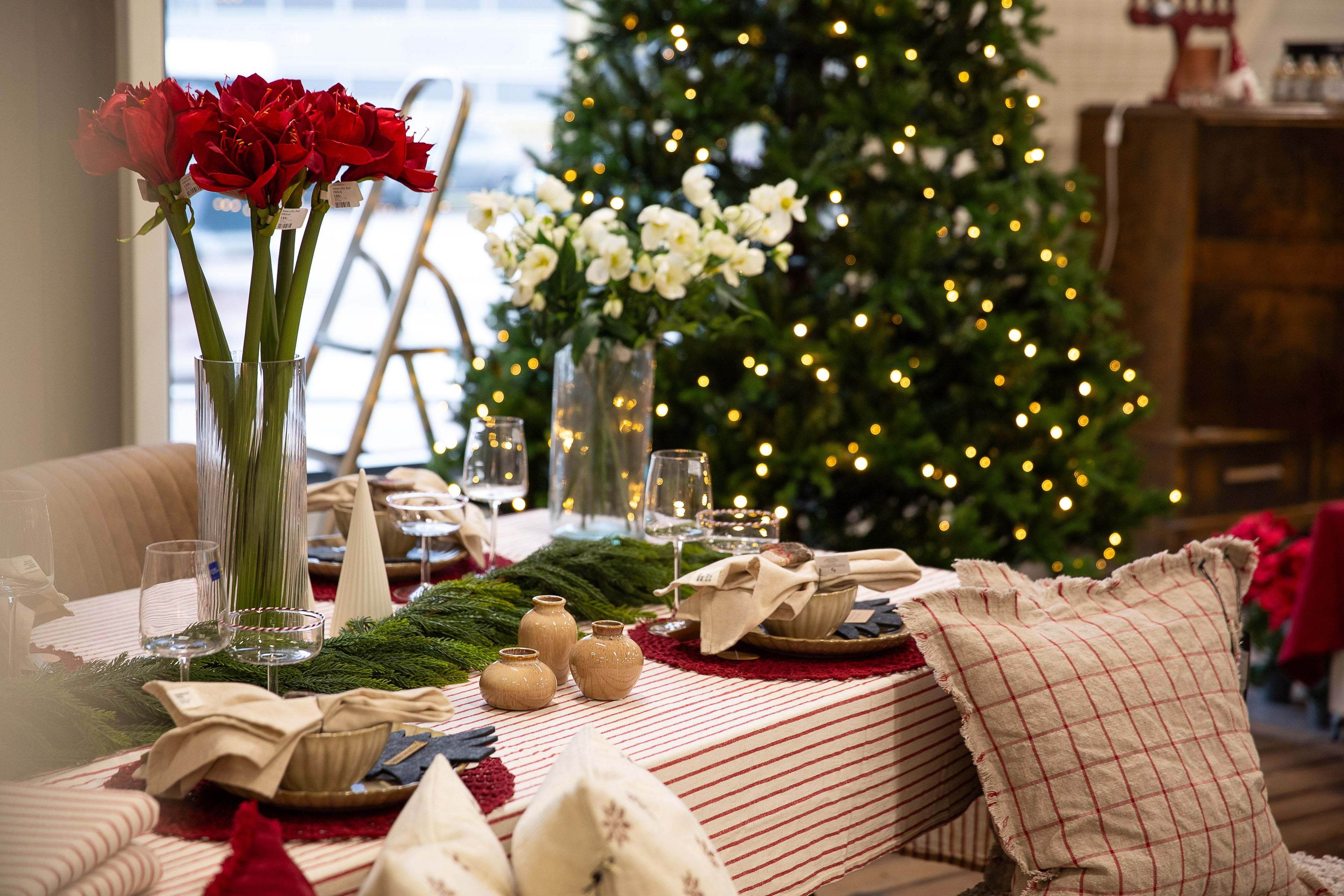 Juldukat bord med röda och vita blommor, grön löpare och julgran med belysning i bakgrunden