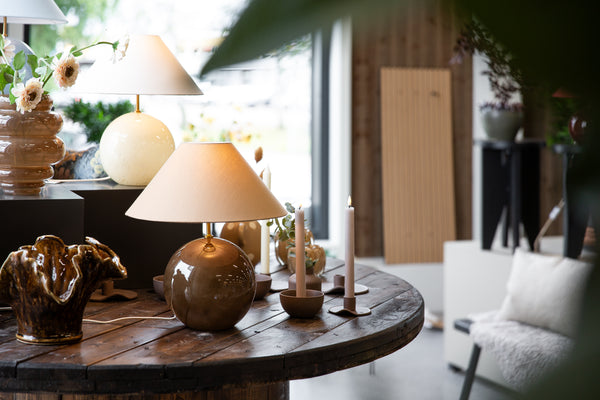 Bordslampa med rund brun bas och vit konformad skärm på träbord med ljusstakar och dekorationer