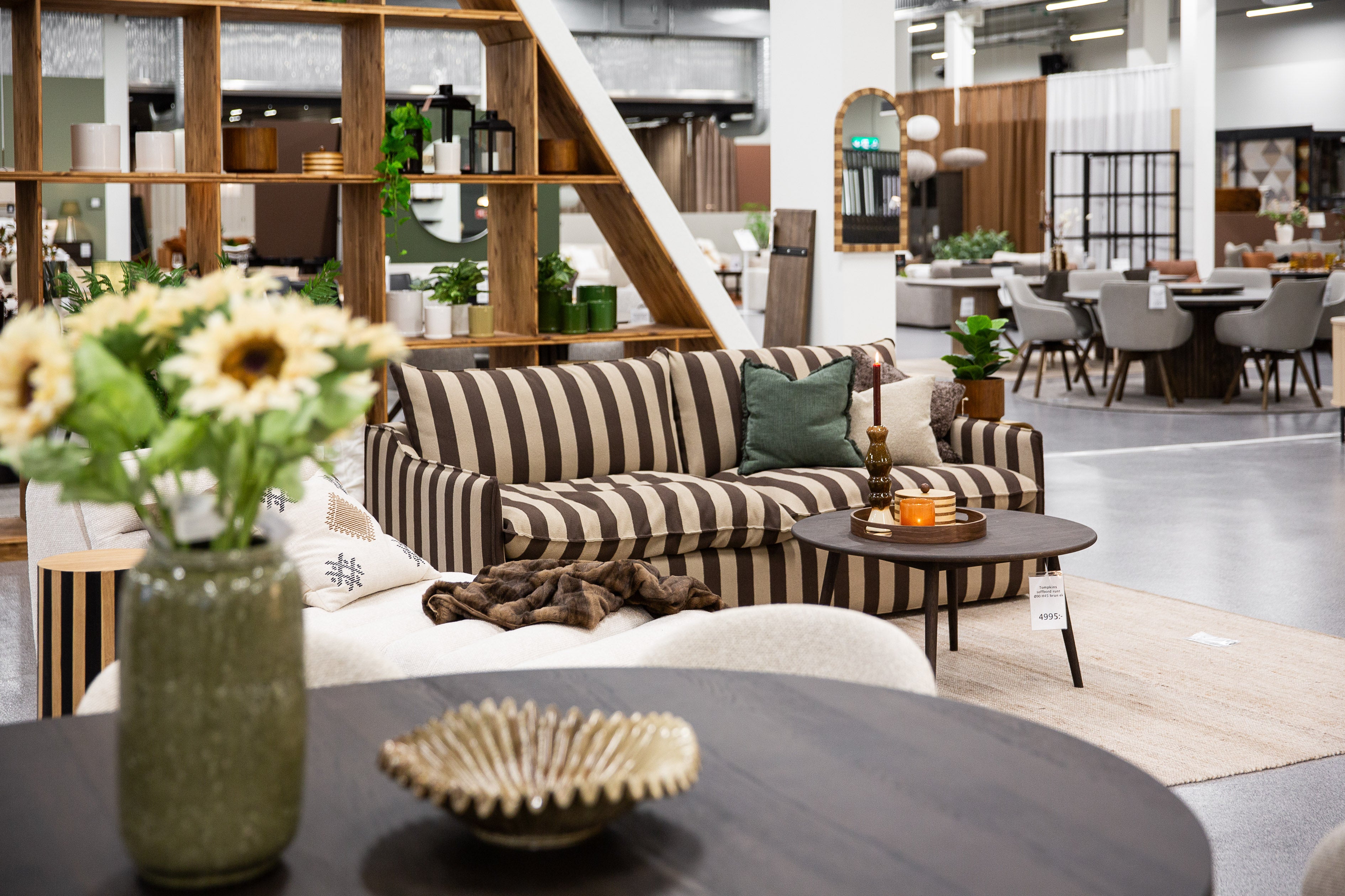 Randig soffa i brun och beige med gröna kuddar i modern möbelutställning med träinredning