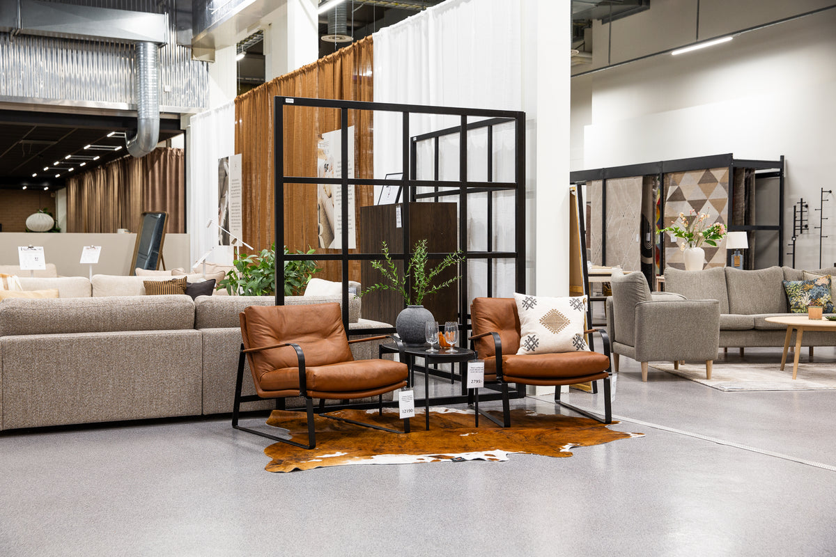 Möbelshowroom med bruna läderfåtöljer, beige soffor och svart rumsavdelare på kohidematta