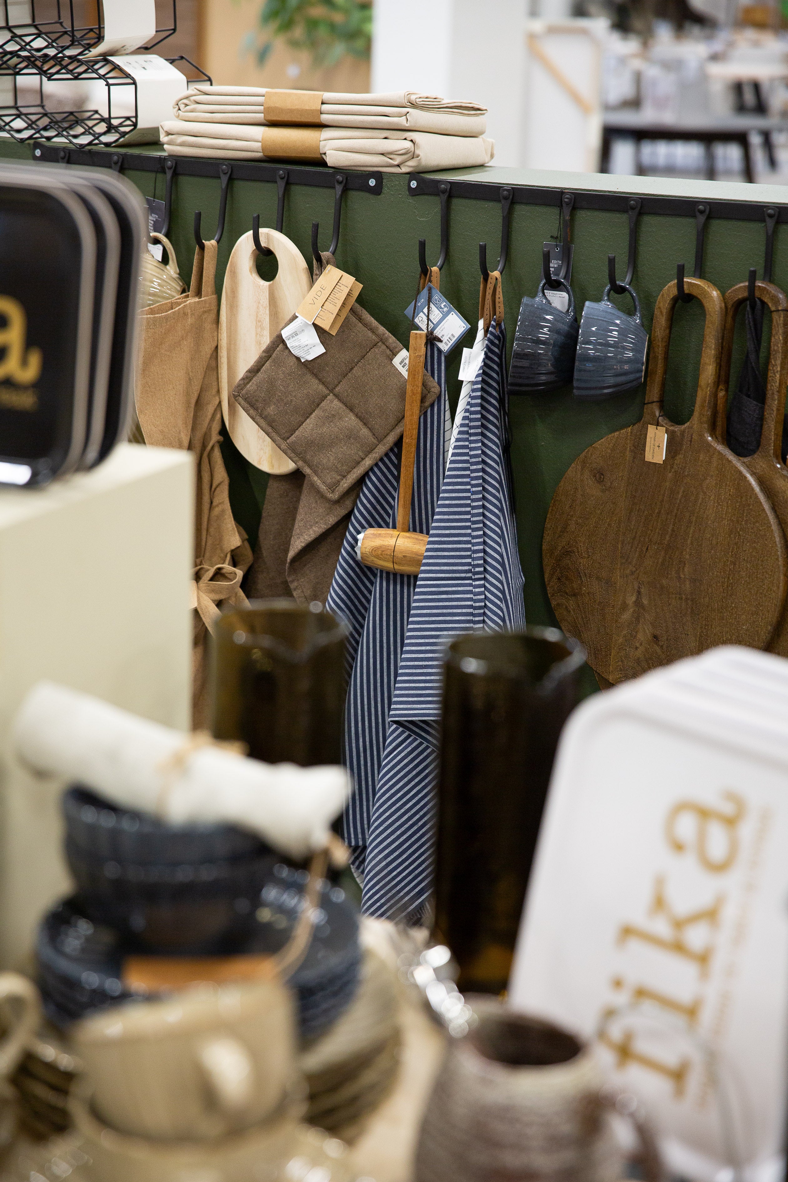 Köksförvaring med krokrad i grönt där kökshanddukar, skärbrädor och grytlappar hänger